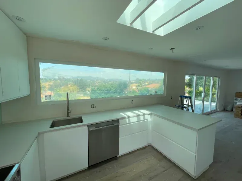 Modern white kitchen with long window overlooking a green landscape and a skylight.