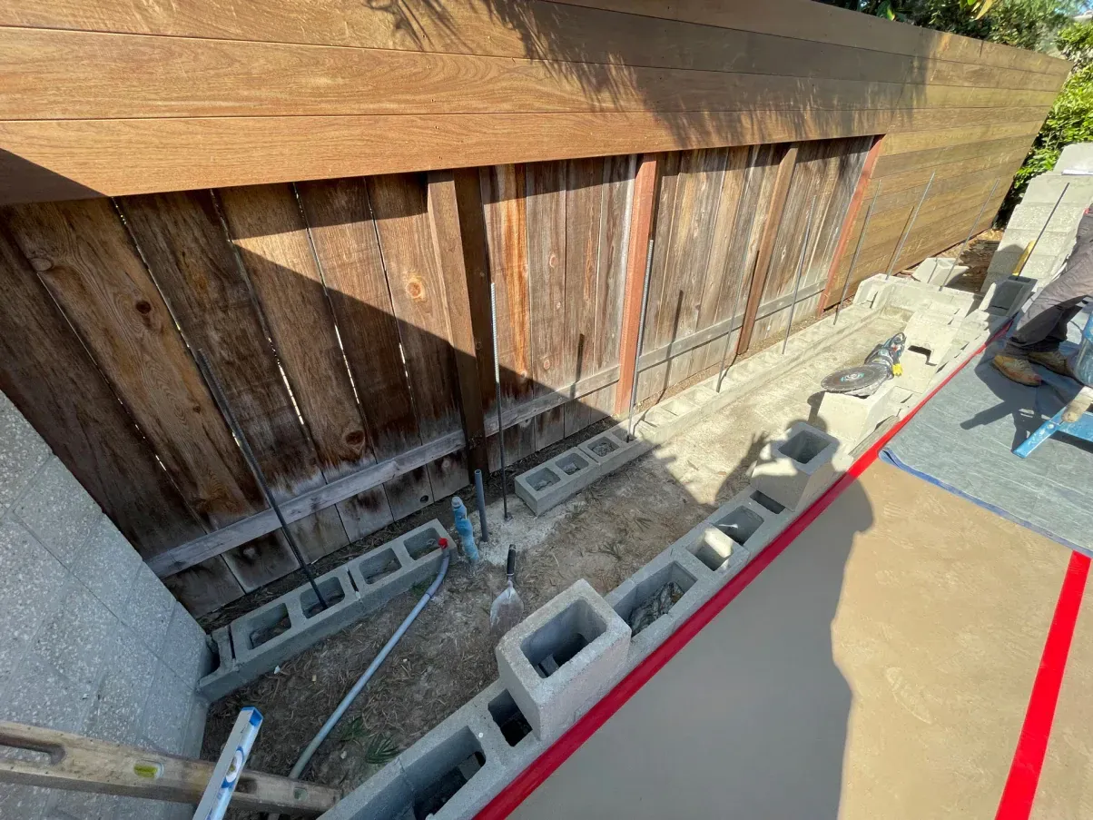 Construction site: cinder blocks and concrete along a wooden fence. A red line marks the edge.