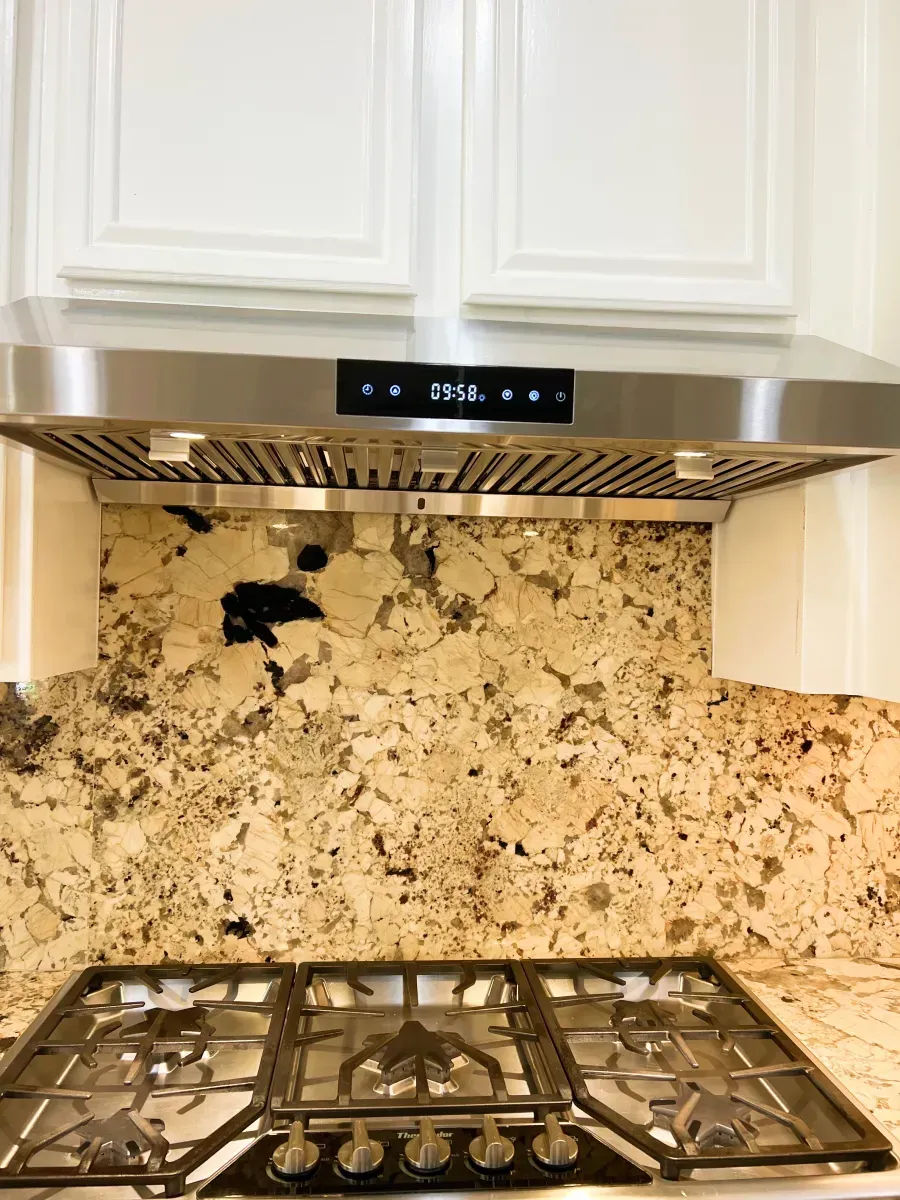 Kitchen with a stainless steel range hood, granite backsplash, and gas stovetop. White cabinets above.