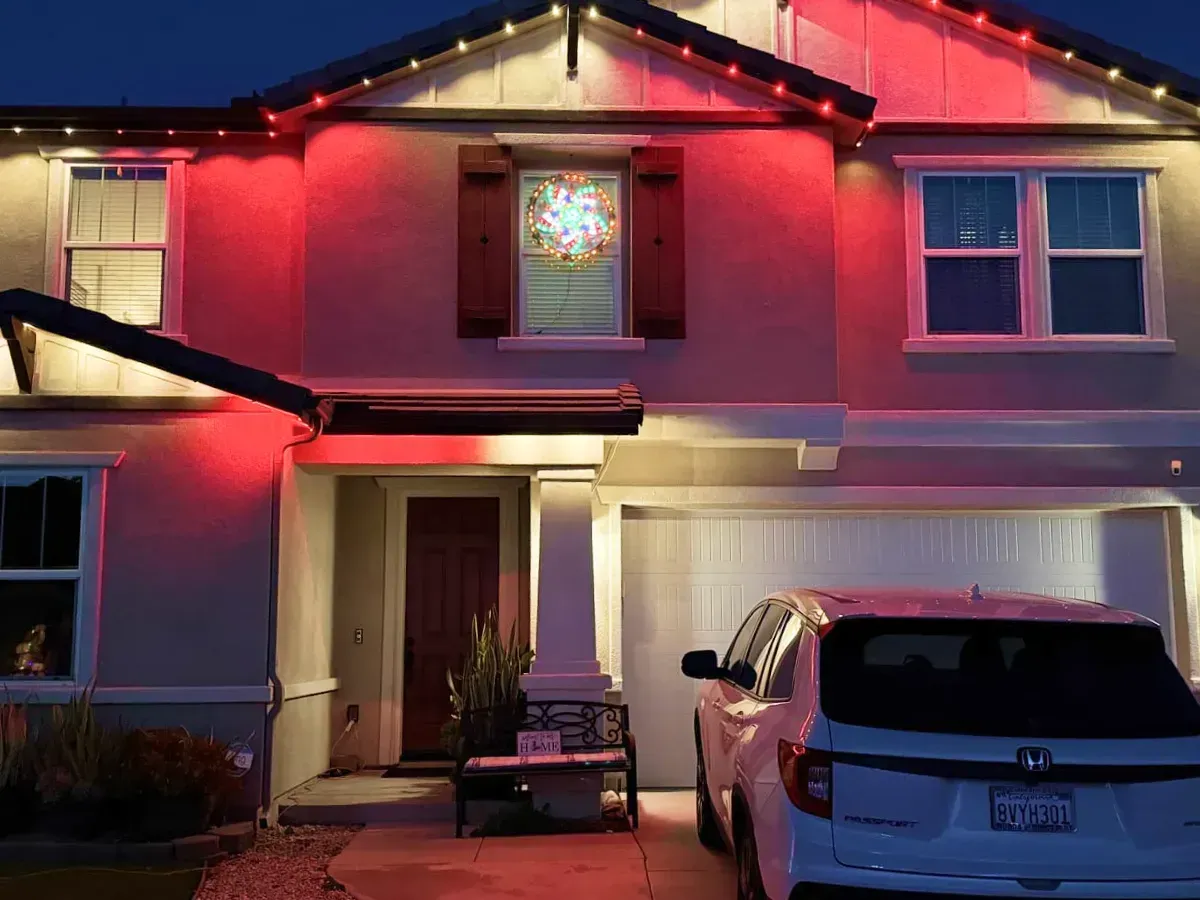 House exterior at night, lit with red lights. A car is parked in the driveway.