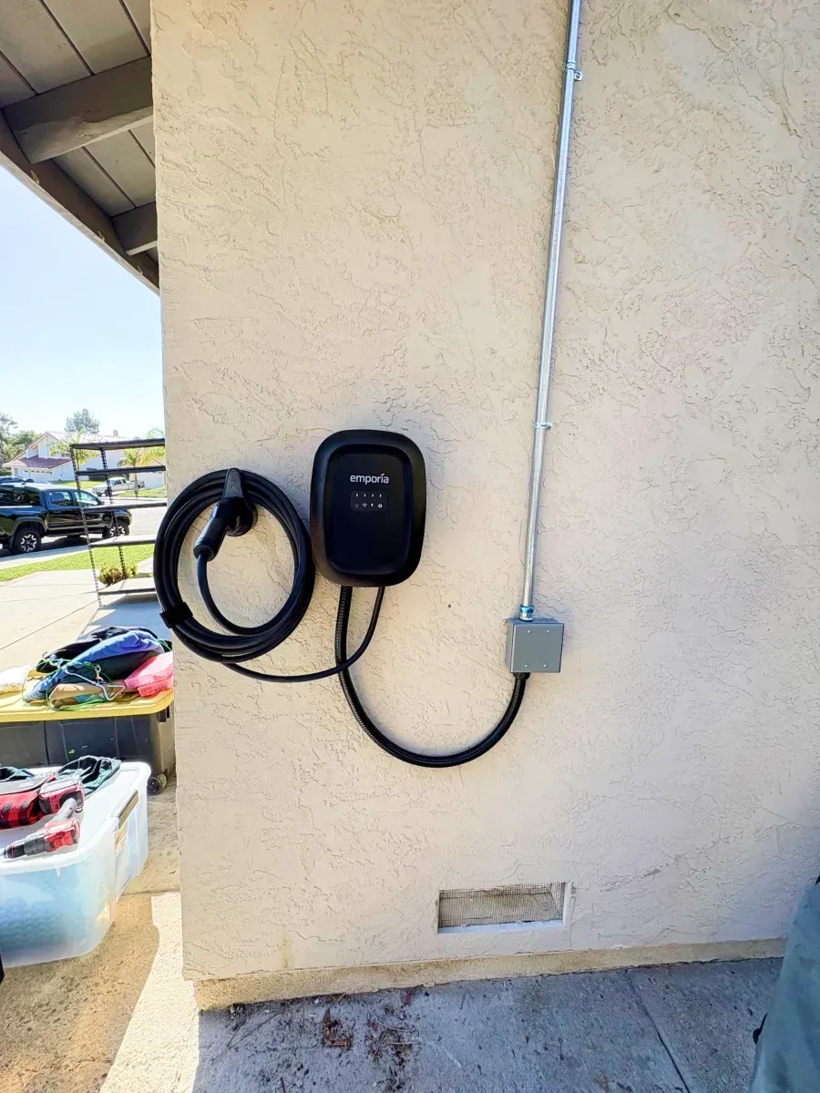 An EV charger mounted on a stucco wall with conduit and a gray cable, outdoors.