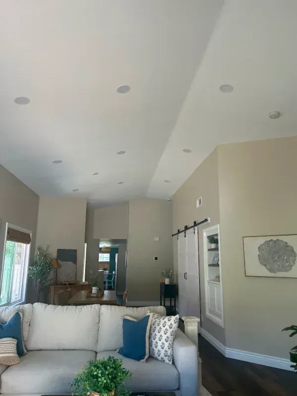 Living room with white sofa, blue pillows, and recessed ceiling lights. Beige walls and dark wooden floors.