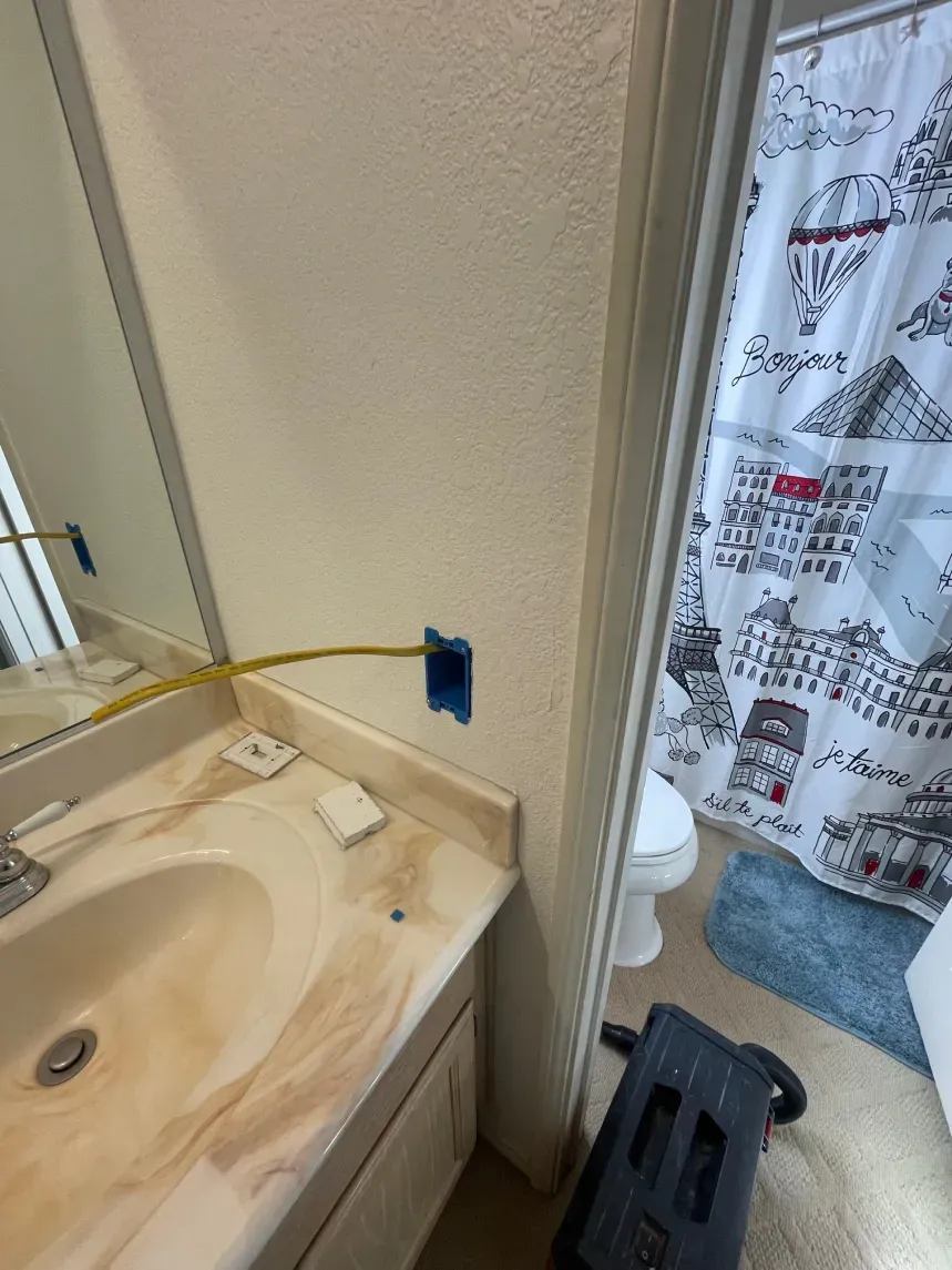 Bathroom with vanity, mirror, and open electrical box on the wall near a door to a shower/toilet.