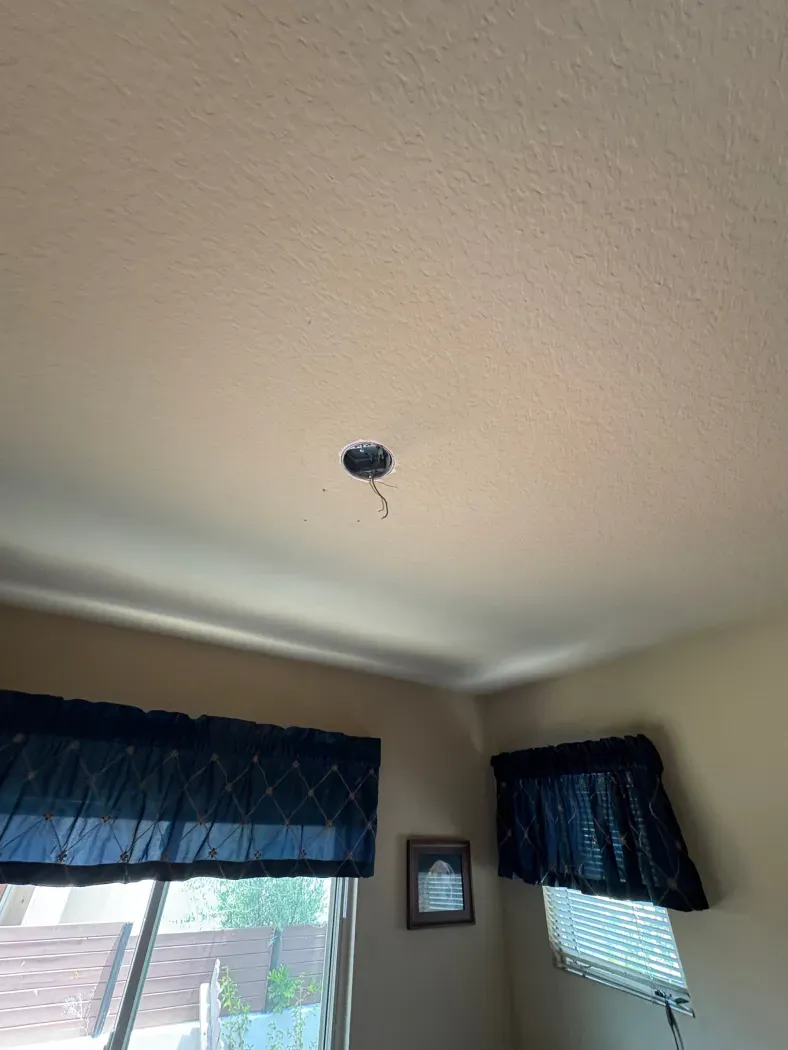 Ceiling with open electrical box and hanging wires, above a window with blue curtains.