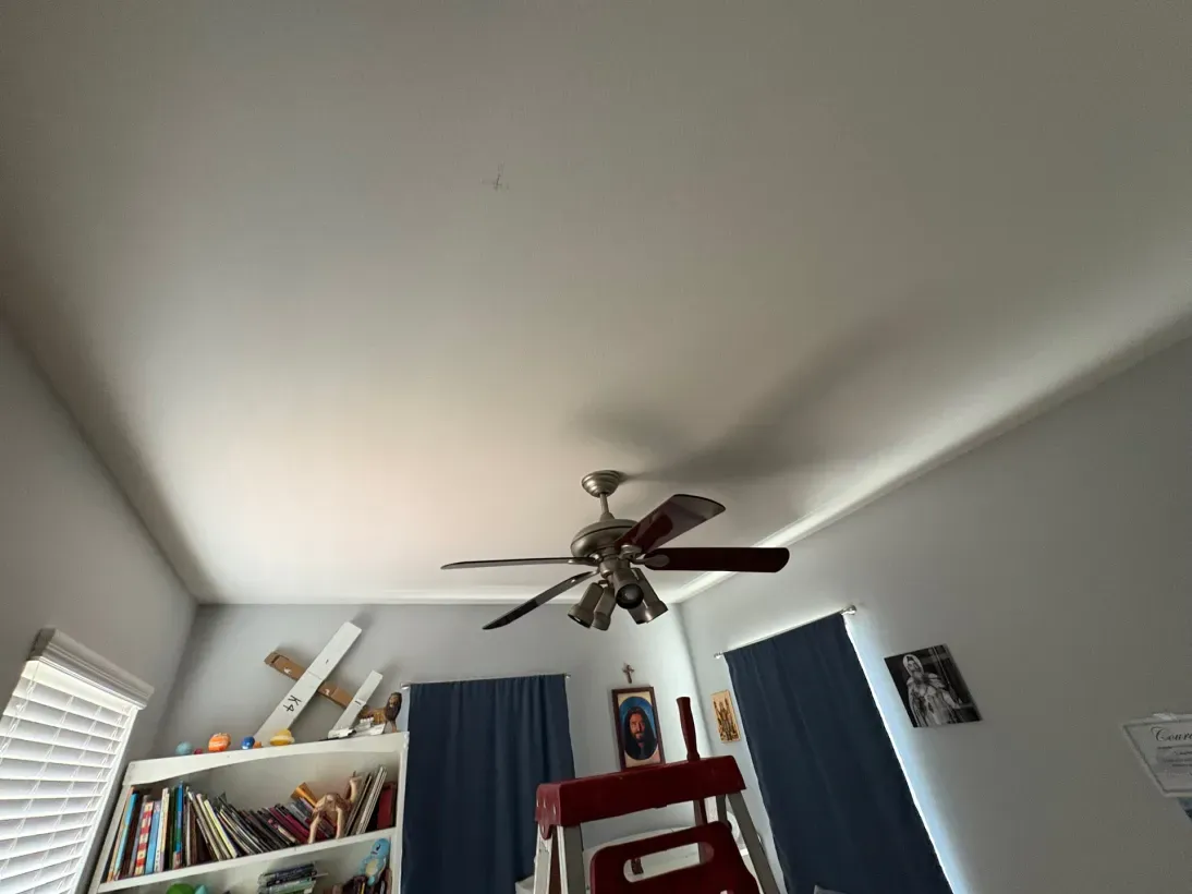 View of a room ceiling, with a fan, bookshelves, window blinds, and curtains.