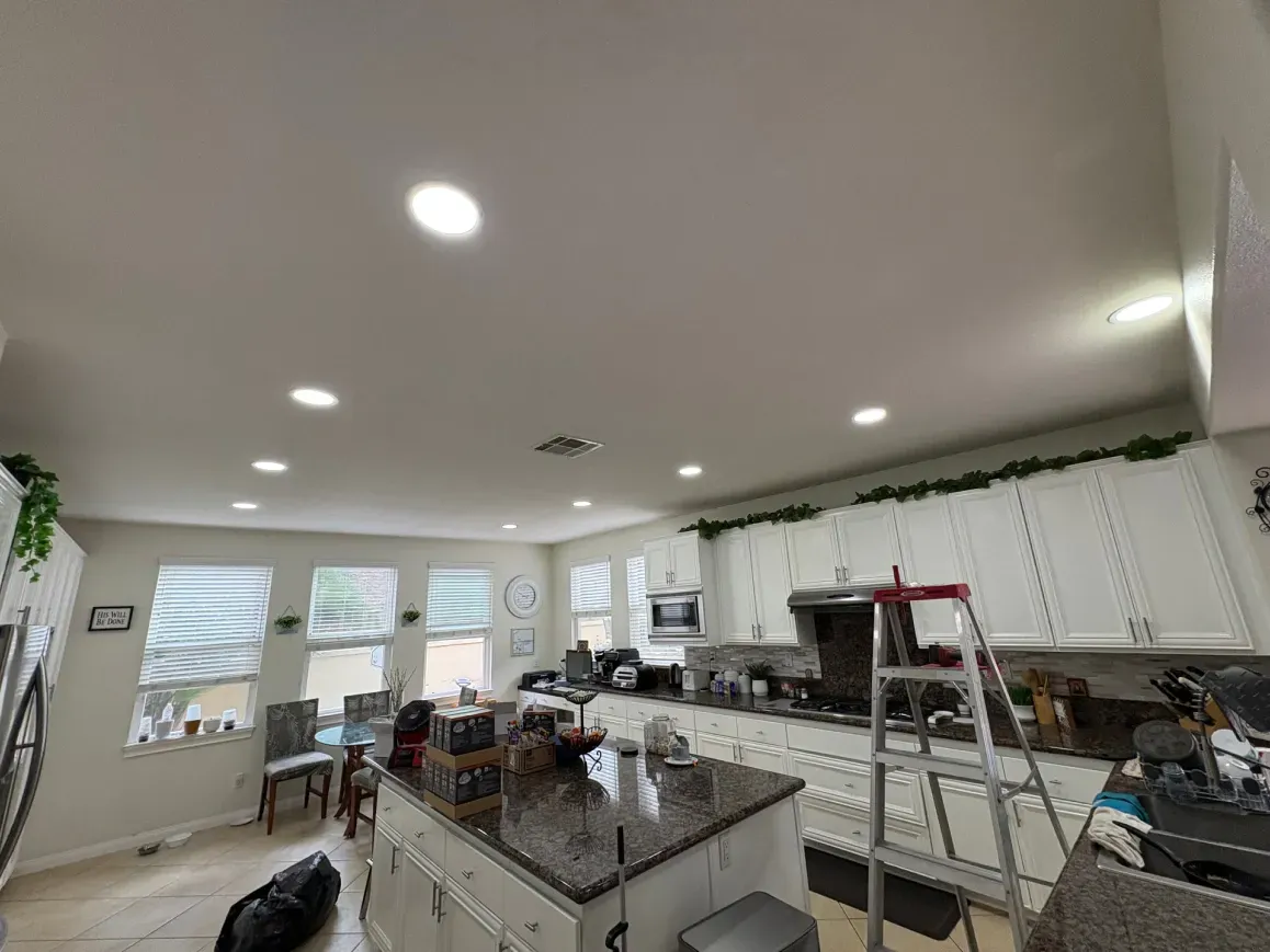 Kitchen interior with white cabinets, island, and recessed lighting. A ladder is present.
