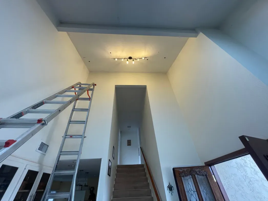 A tall hallway with stairs, ladder, and a light fixture on the ceiling.