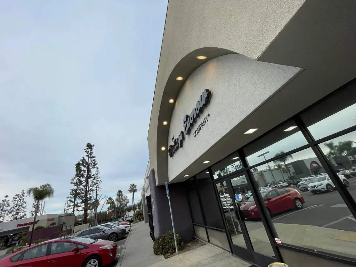 Exterior of a business with sign, reflective windows, red and silver cars parked outside. Gray and white building.