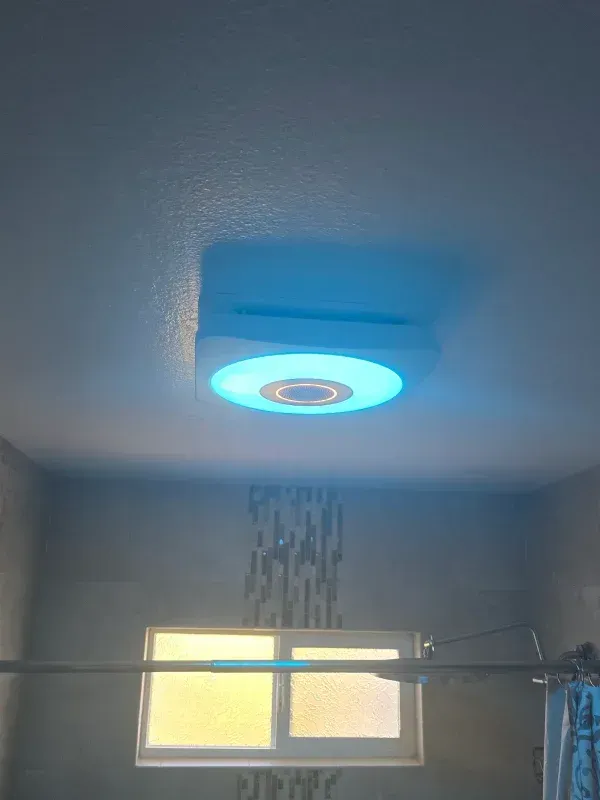 Bathroom ceiling light emitting blue light, over a window and shower.