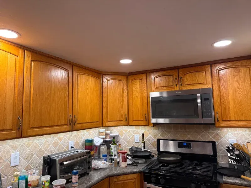 Kitchen with oak cabinets, stainless steel microwave and stove, beige backsplash, and recessed lighting.