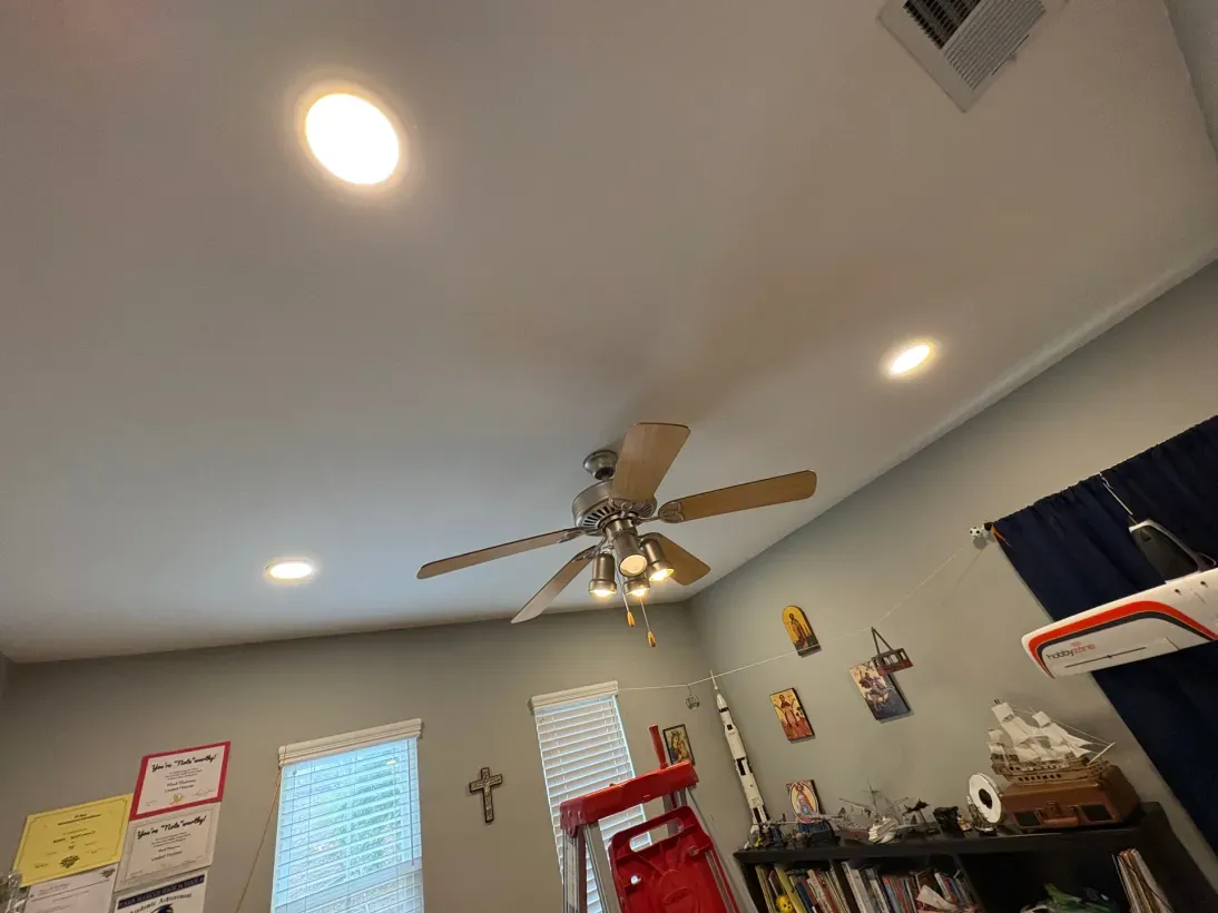 Ceiling with recessed lights and a fan; small room with artwork, red chair, and a window.