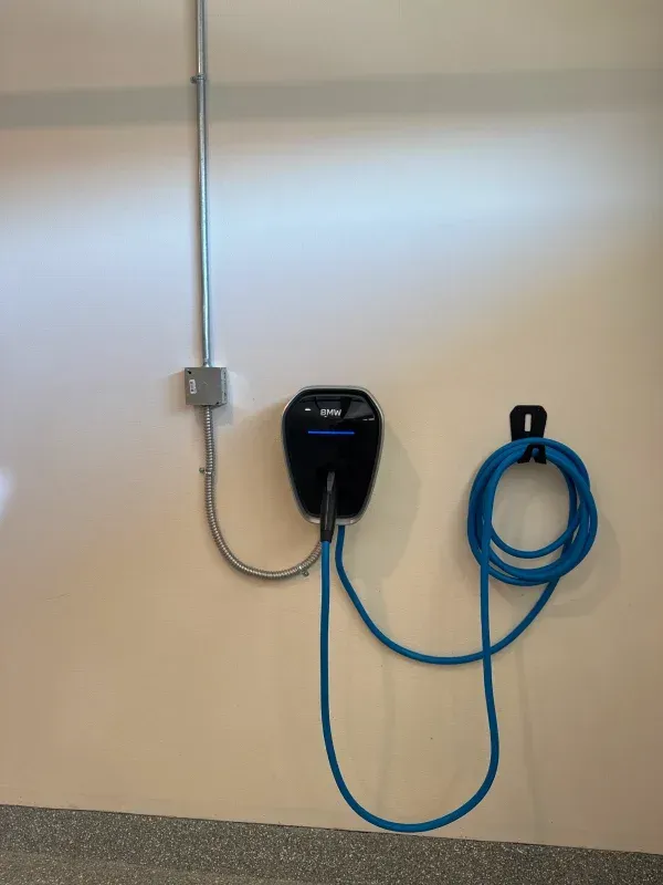 Electric vehicle charger mounted on a wall with cable and conduit, blue, gray, and silver.