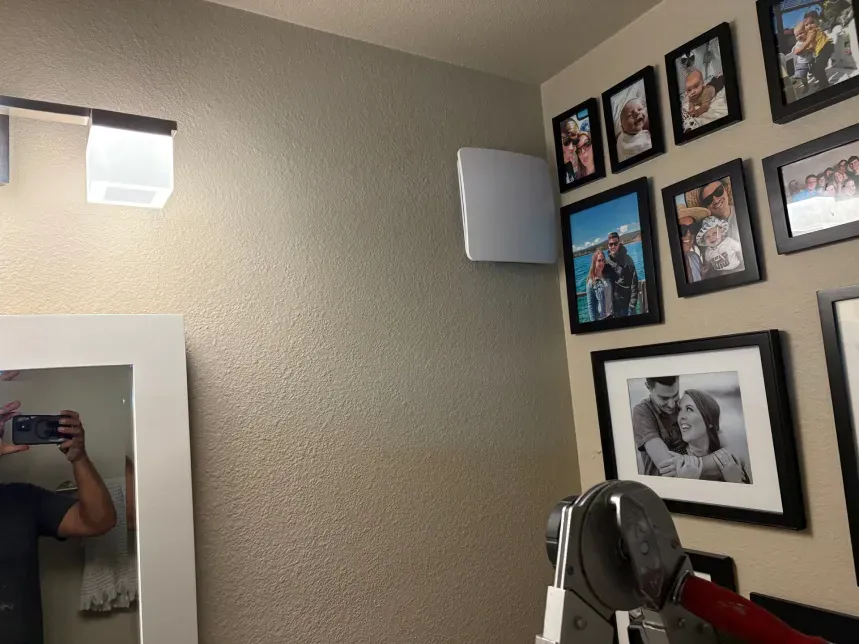 A bathroom with a mirror and framed photos on the wall. A speaker is mounted on the wall.