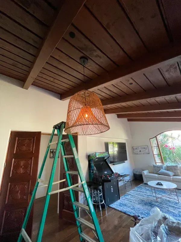 Ladder near a woven pendant light fixture hanging from a wood ceiling in a room.