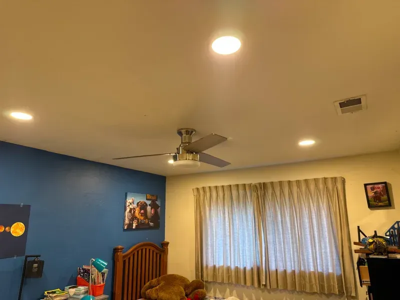 Bedroom with ceiling fan, recessed lights, blue wall, curtains, bed, and artwork.