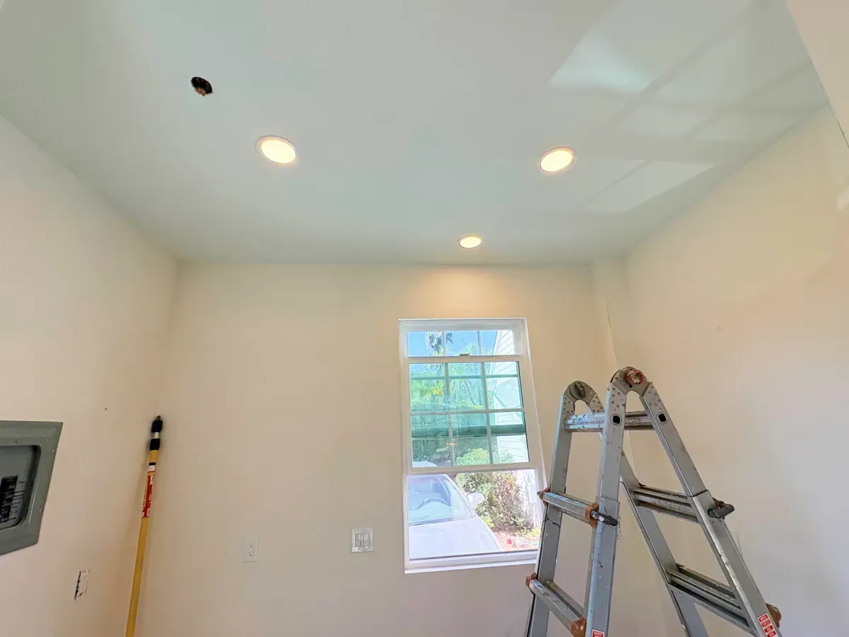 Interior view of a room with a window, recessed ceiling lights, a ladder, and electrical box.