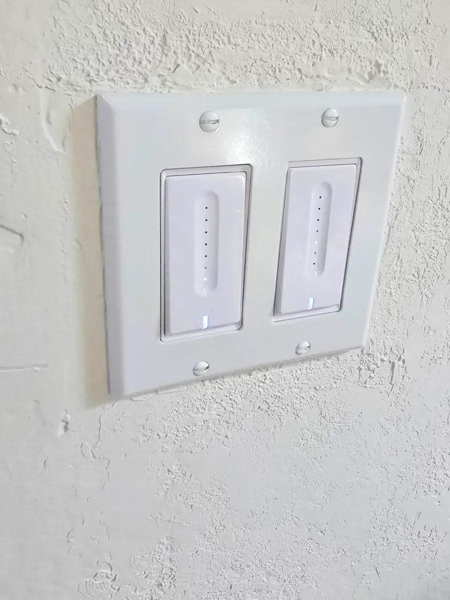White light switch plate with two smart light switches on a textured white wall.
