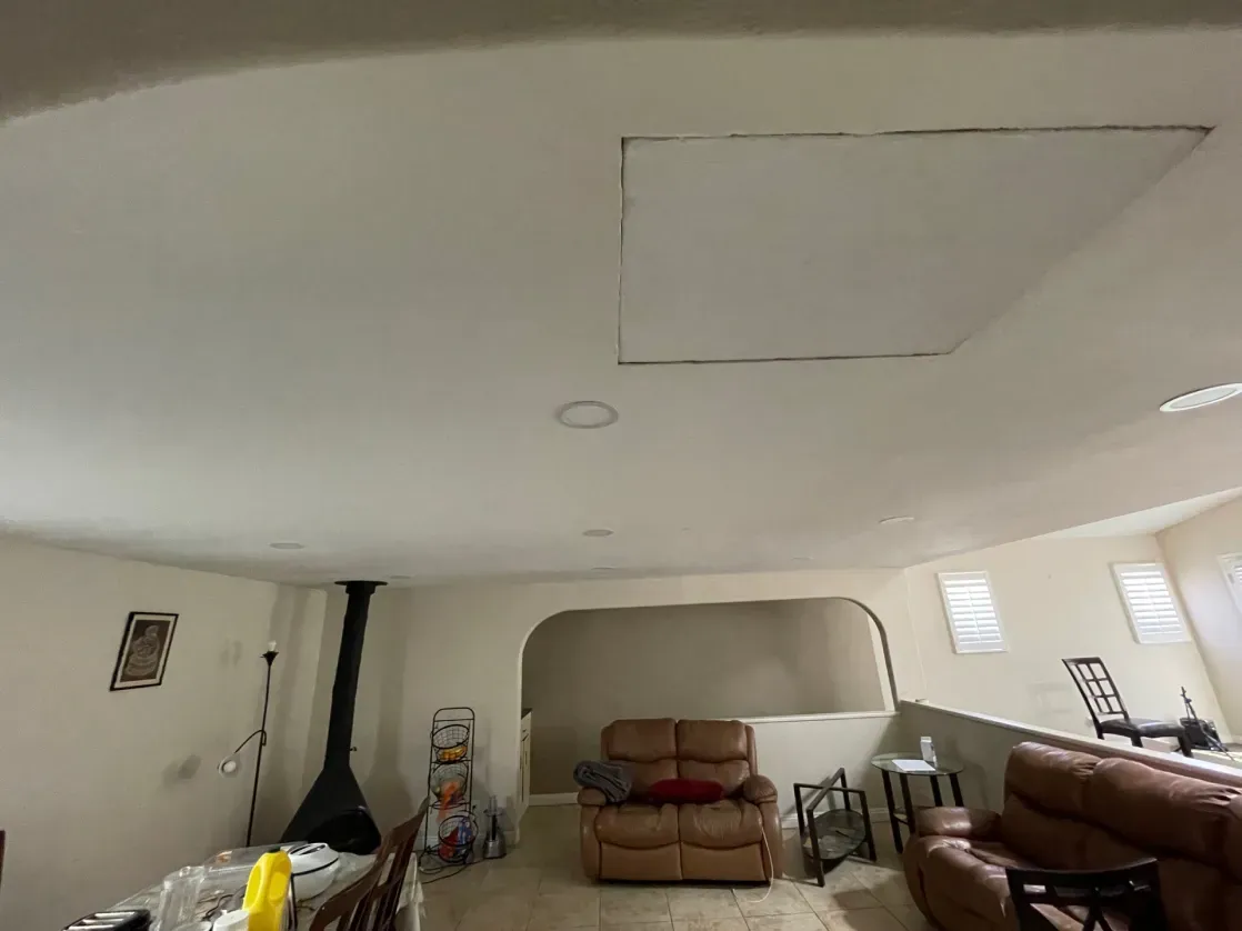 Interior view of a living room with a fireplace, archway, and leather furniture. A ceiling access panel is visible.