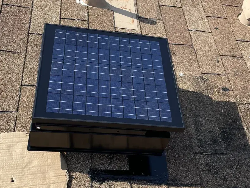 Solar-powered roof vent installed on a shingled roof, featuring a dark solar panel and a black frame.