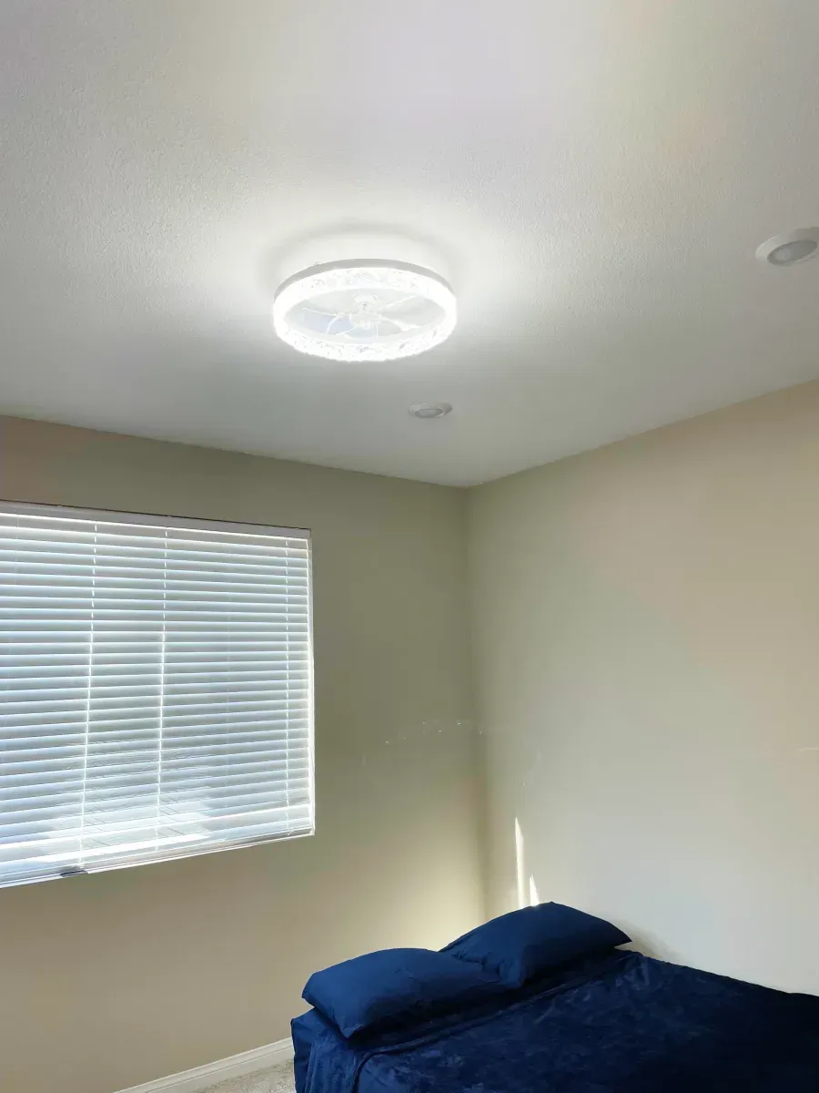Bedroom with a blue bed, blinds on a window, and a bright ceiling light.