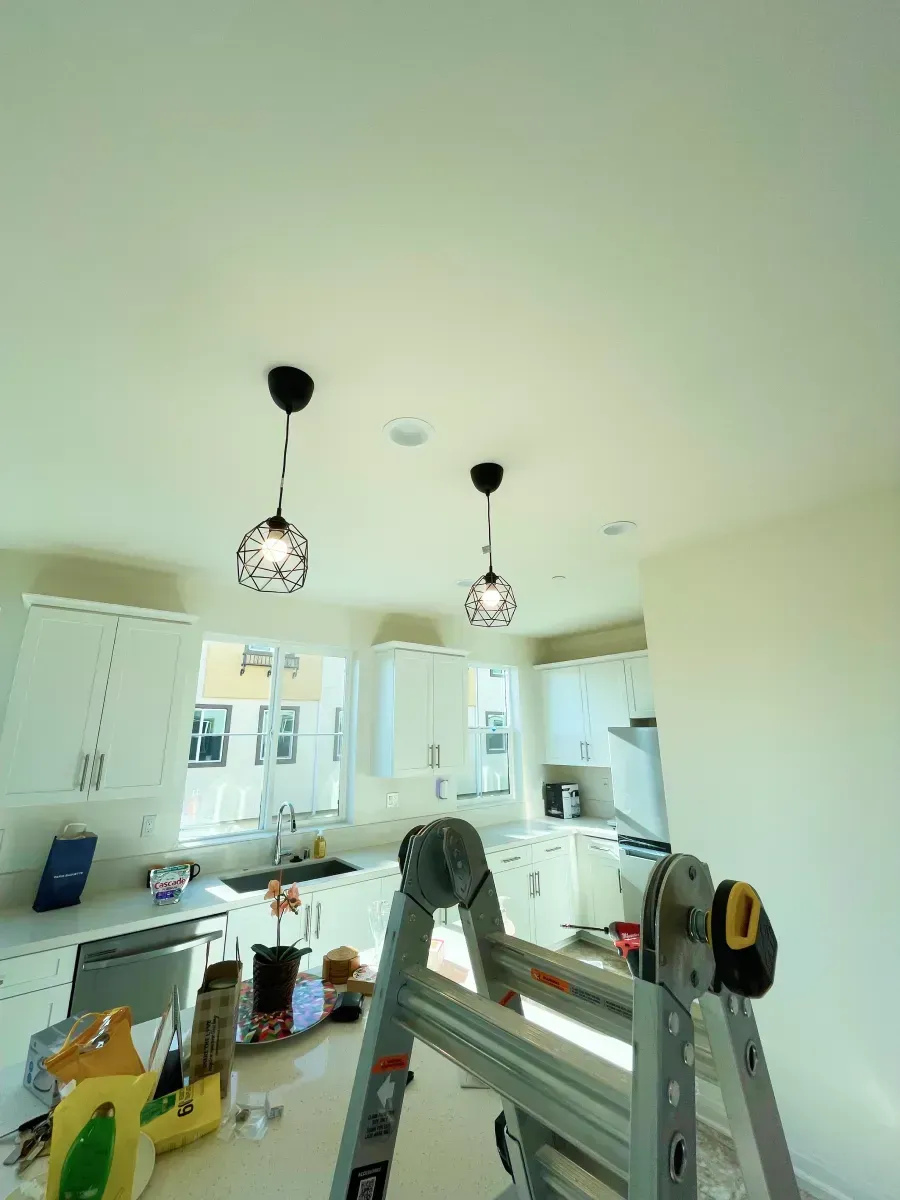 Kitchen with two pendant lights, cabinets, and a ladder.