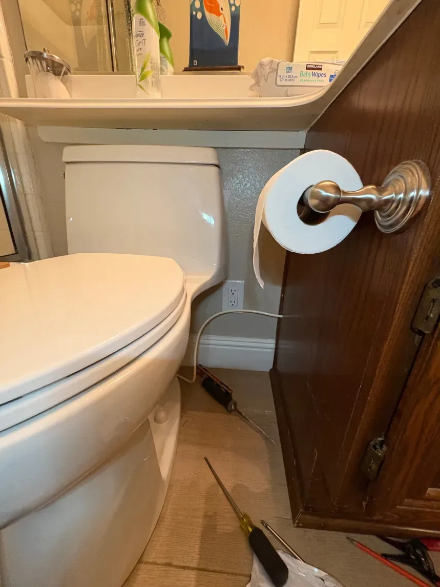 Toilet in a bathroom next to a wooden cabinet. Screwdrivers are on the floor.
