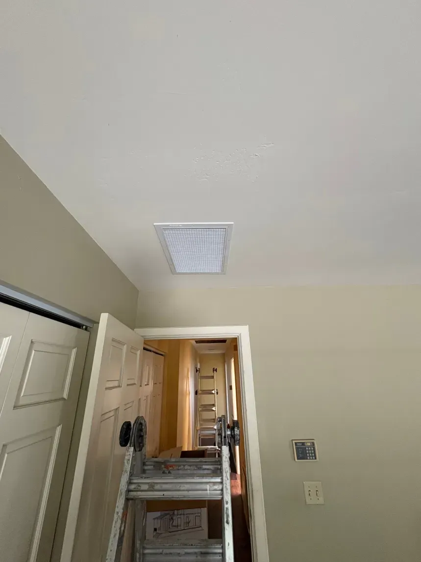 Hallway ceiling with HVAC vent, a partially open door, and a stepladder. Beige walls and white ceiling.