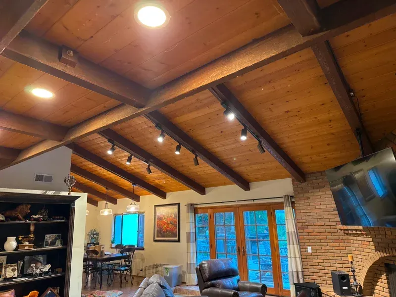 Wooden ceiling with beams and track lighting in a living room; French doors, brick fireplace, and shelves.