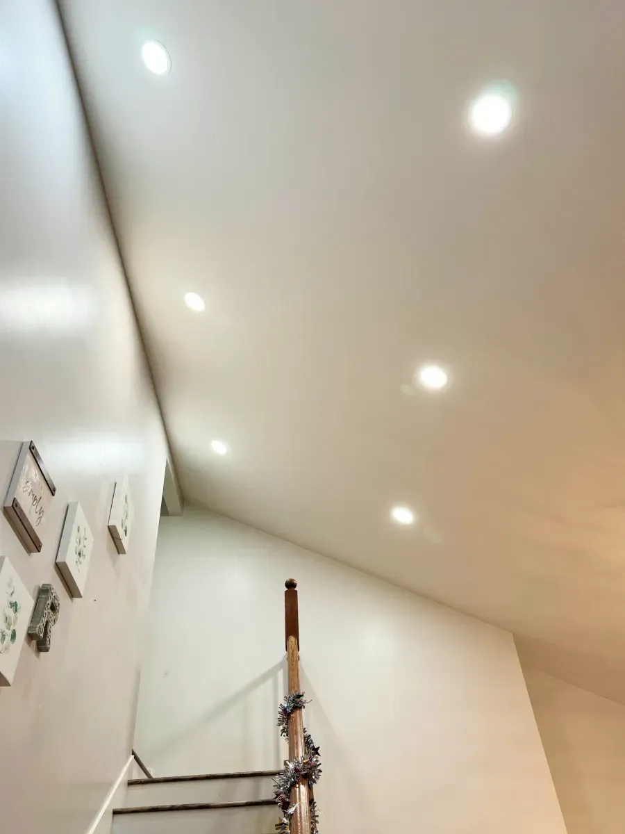 Stairway interior with recessed ceiling lights. White walls, wooden handrail, and art on the left wall.