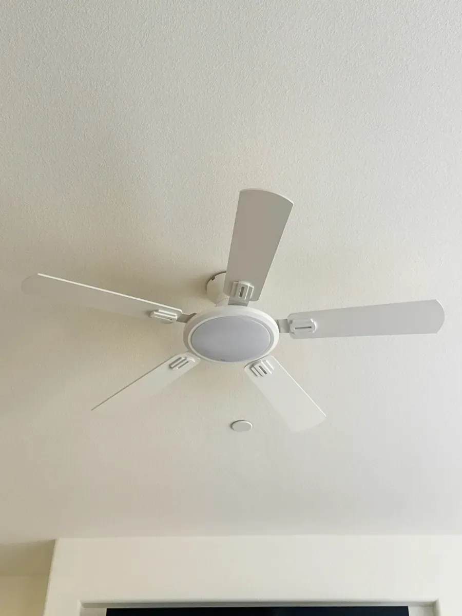 White ceiling fan with light fixture. Blades are angled, and it's mounted on a white ceiling.