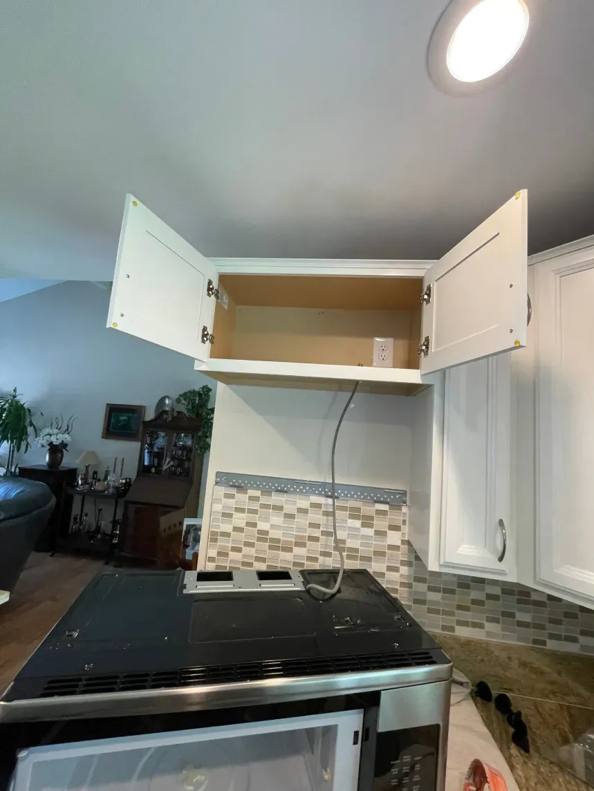 Kitchen cabinet with open doors above an electric range and microwave. White cabinets, tan backsplash.