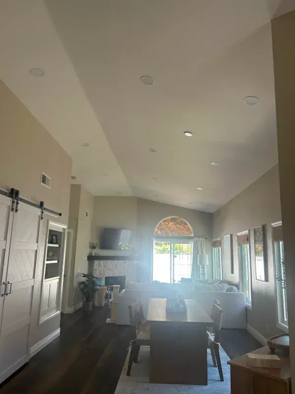 Spacious living room with recessed lighting, dark wood floors, white walls, and a large window.