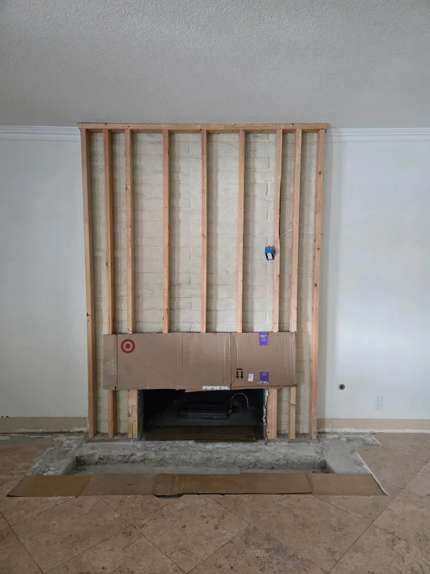 Fireplace under construction, framed with wood studs. Concrete hearth and sheetrock visible.