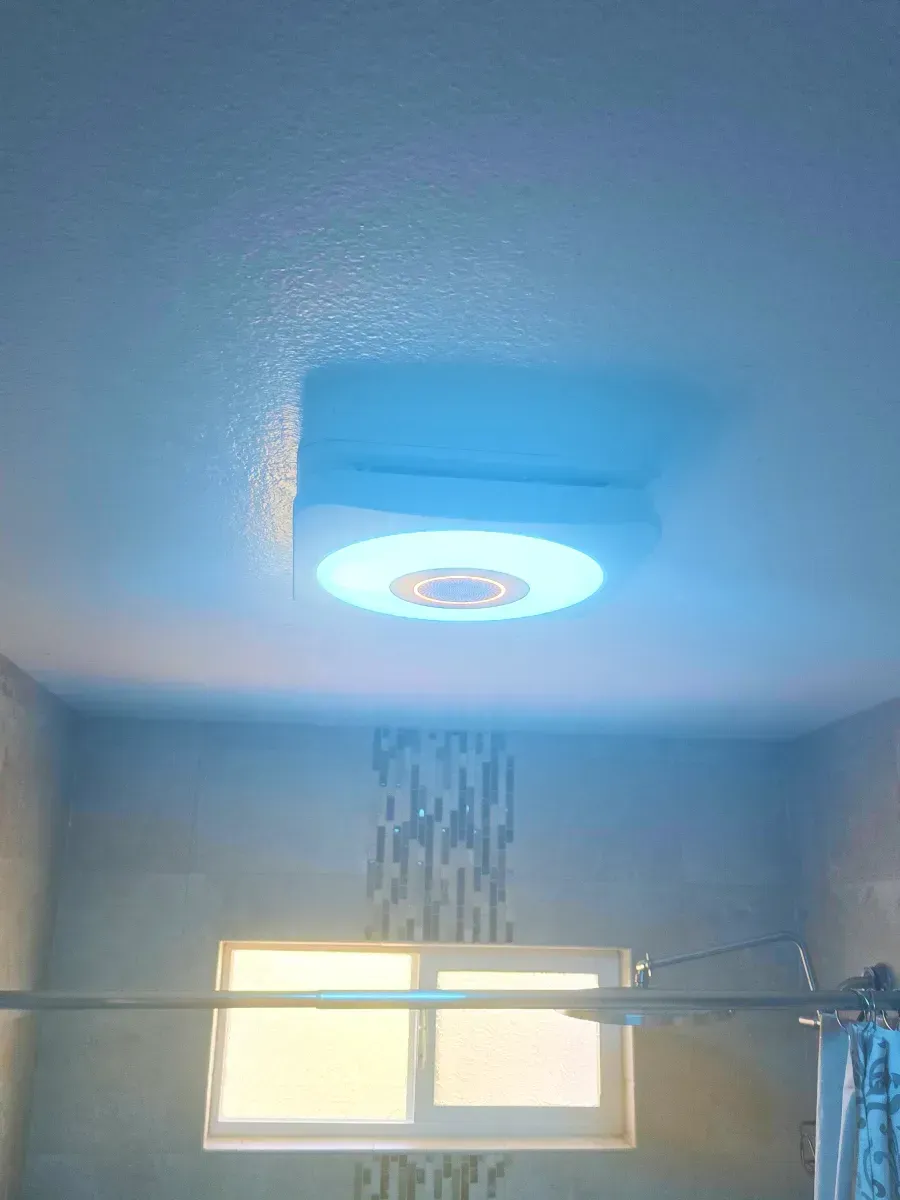 Bathroom ceiling light emitting blue light, over a window and shower rod.