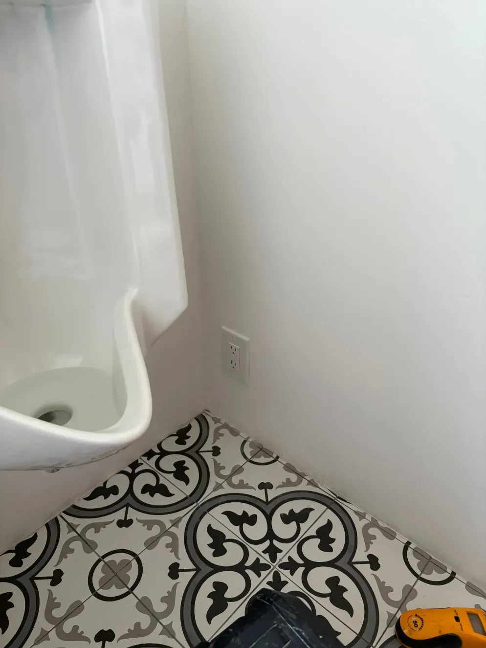 Bathroom corner with a white sink, patterned floor tiles, and an electrical outlet on the white wall.