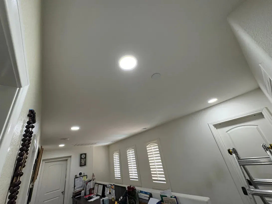 Bright hallway with white walls and ceiling, recessed lights, and a closed door.