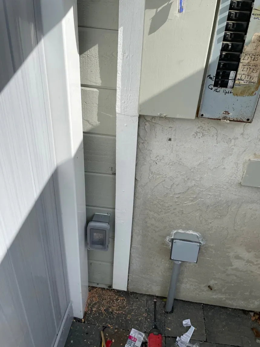 Electrical conduit runs vertically beside a wall with electrical boxes and a breaker box.