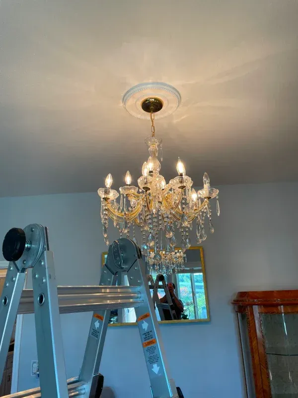 Chandelier hanging from ceiling, above a ladder. A person's reflection visible in a mirror below.