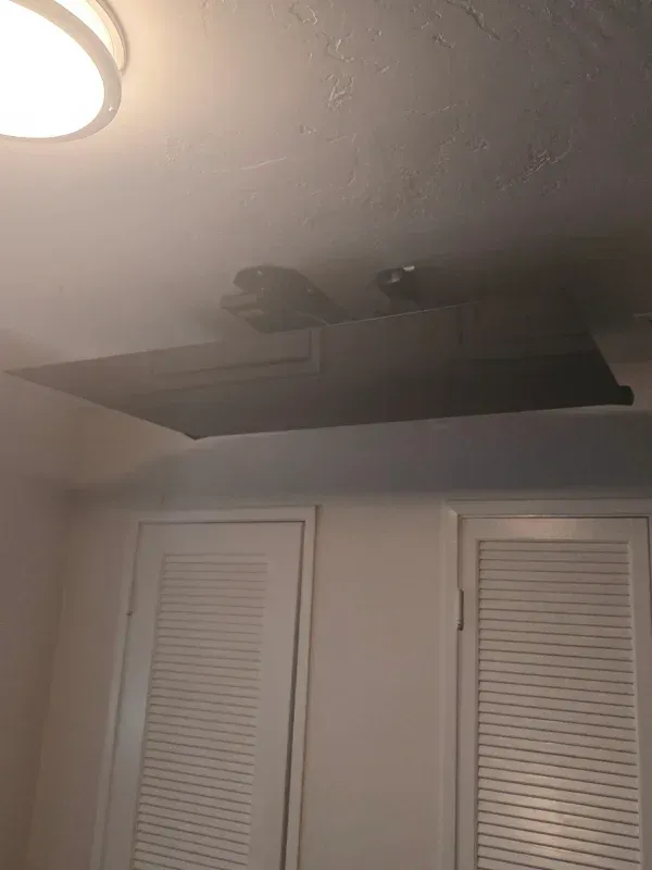 A dark, rectangular ceiling-mounted projector screen is lowered in a room with two white louvered doors.