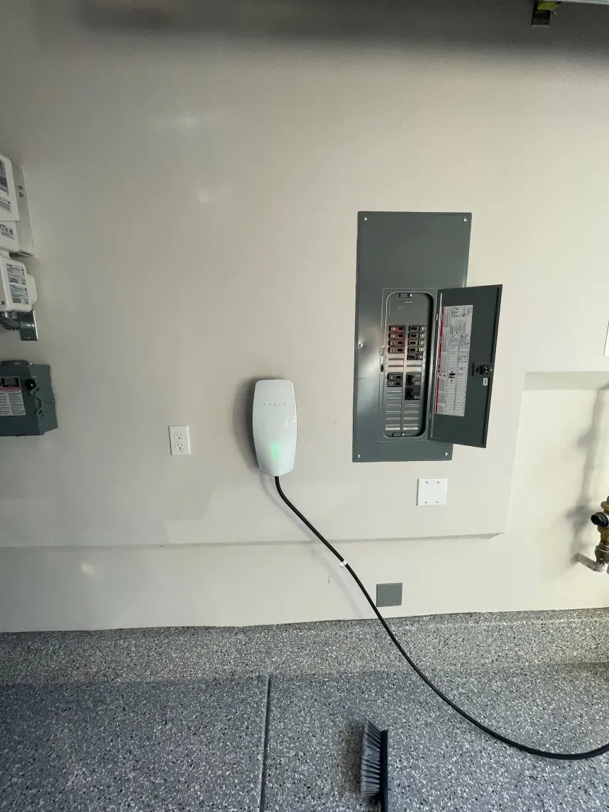 Electric vehicle charger next to a gray electrical panel in a garage.