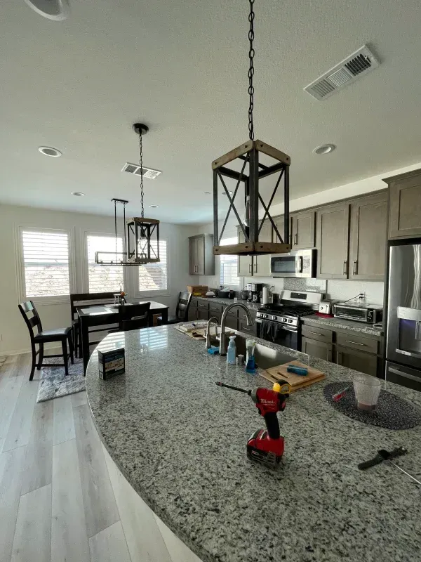 Kitchen with granite island and hanging lights. Stainless steel appliances and dining table visible.