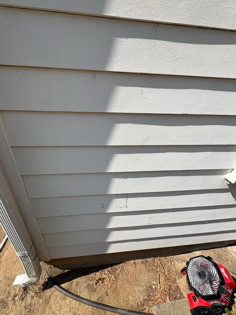 White siding on a house, with visible shadows and a glimpse of a black hose and a toy car.