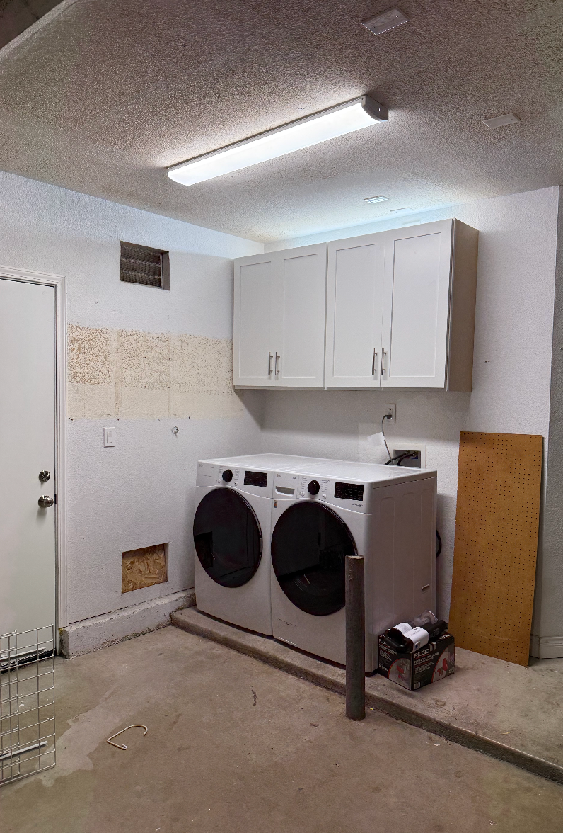 Laundry room with washer and dryer, upper cabinets, and a door on the left.