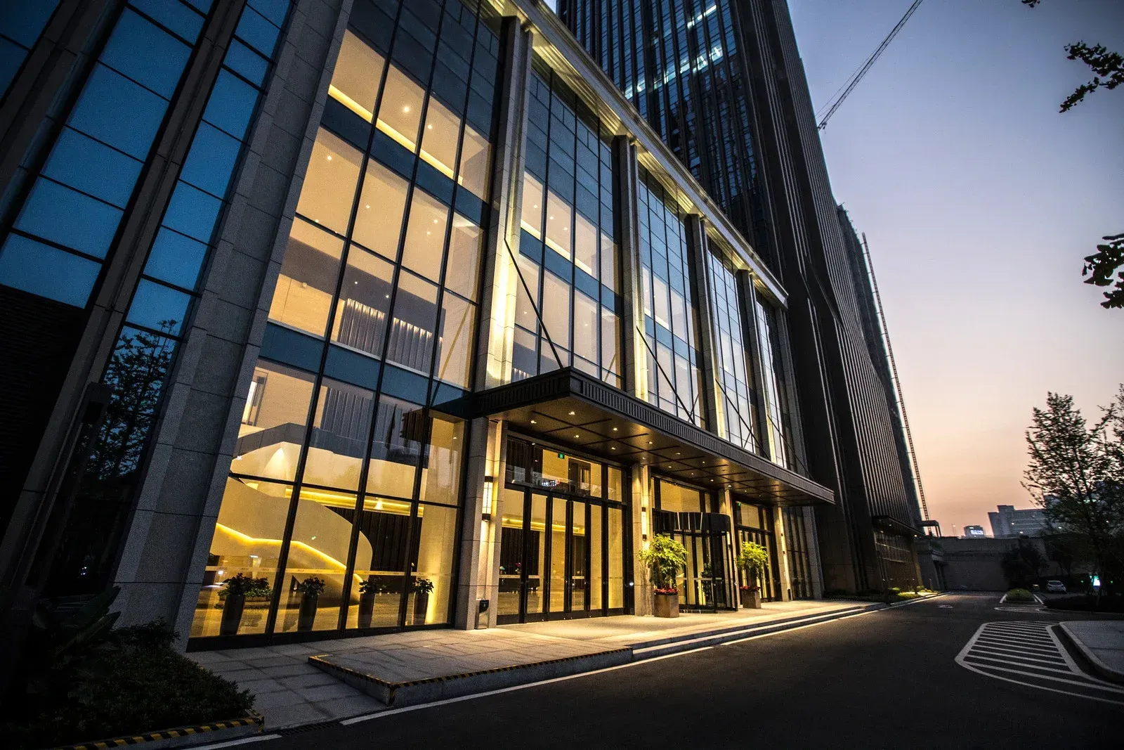 Modern office building entrance with glass walls and warm interior lighting. Dusk setting.