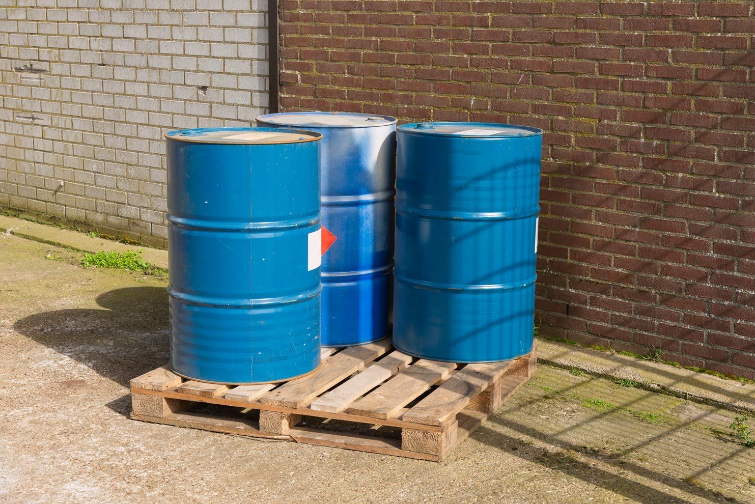 Three blue colored oil barrels placed outside on a wooden pallet