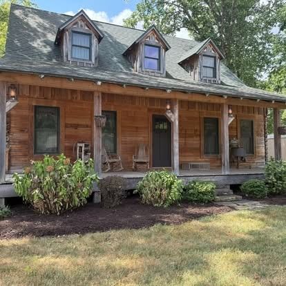 Rustic wooden cabin with porch, three dormers, and landscaping.