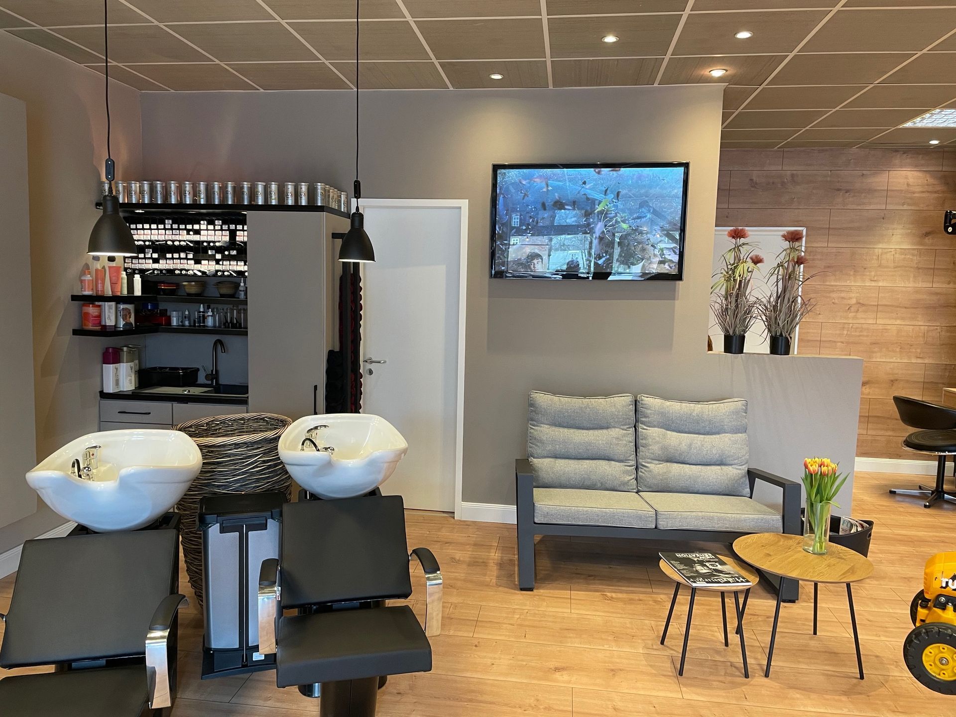 Ein Salon mit Couch, Stühlen, Waschbecken und einem Fernseher an der Wand.