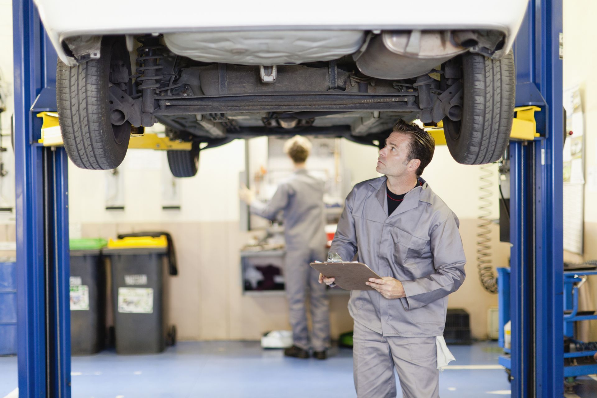 A man is standing under a car on a lift in a garage.