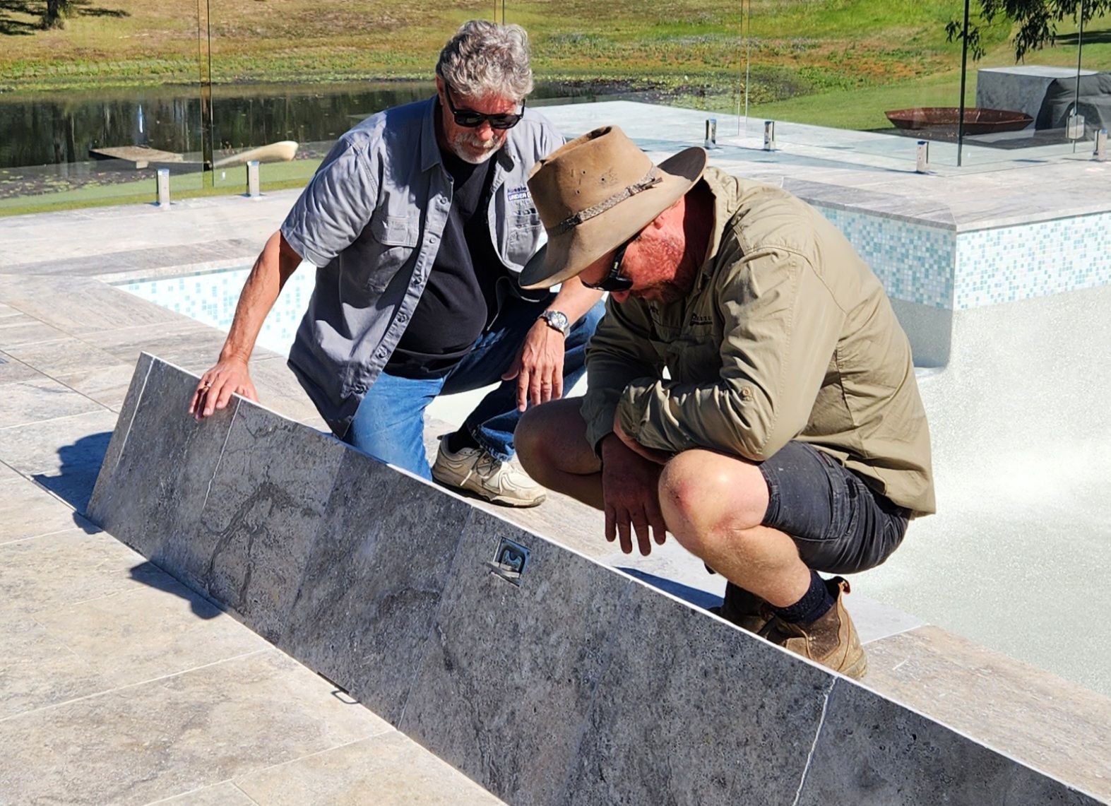 Two men inspecting a long, gray tile near a pool; one man wears a hat and squats  — Aussie UnderCover In South Nowra, NSW