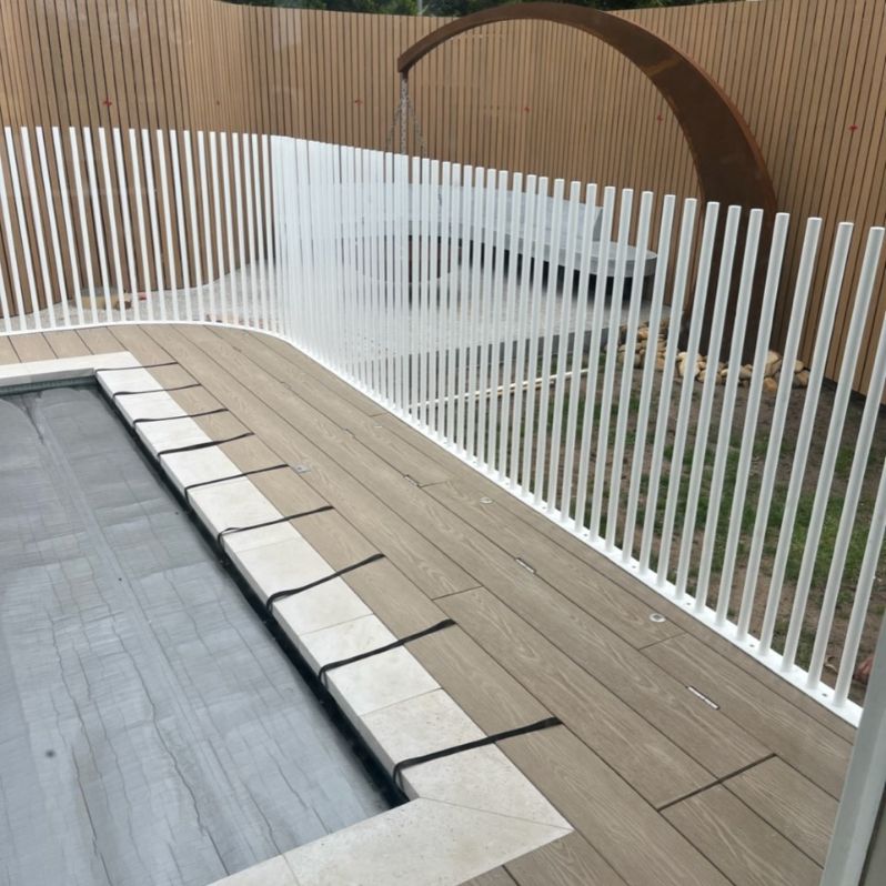 A swimming pool surrounded by a white fence and a wooden deck.